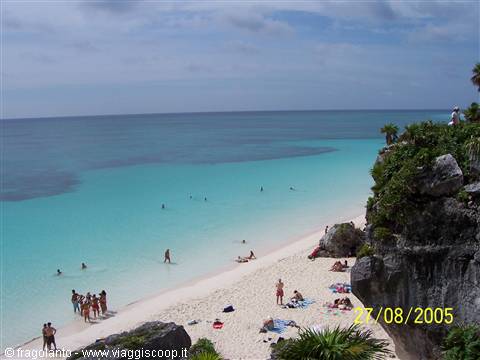 Tulum beach: rocky cliff, white sand and swimmers in turquoise water