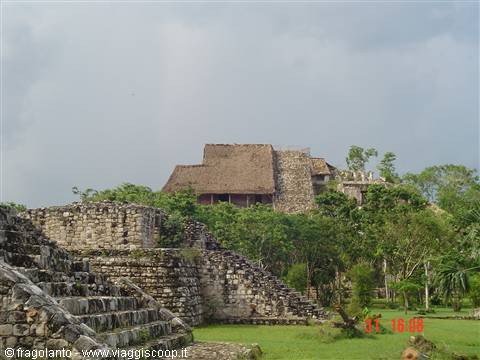 Mayan stone ruins with thatched pyramid roof under cloudy sky