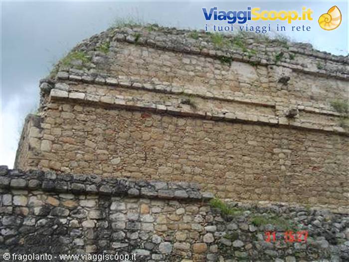 Mayan dry-stone pyramid under a cloudy sky, grass between the blocks