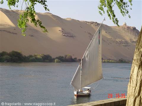 White-sailed felucca glides on the Nile before Aswan's sand dunes