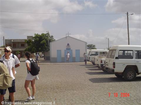 Tourists near a small white church with blue doors and parked jeeps