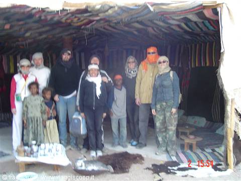 Tourists and Bedouins pose inside a colorful fabric tent, desert camp