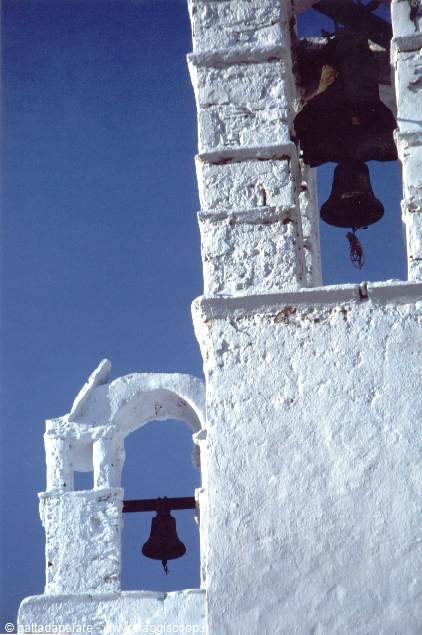 Whitewashed bell tower with bronze bells against deep blue sky