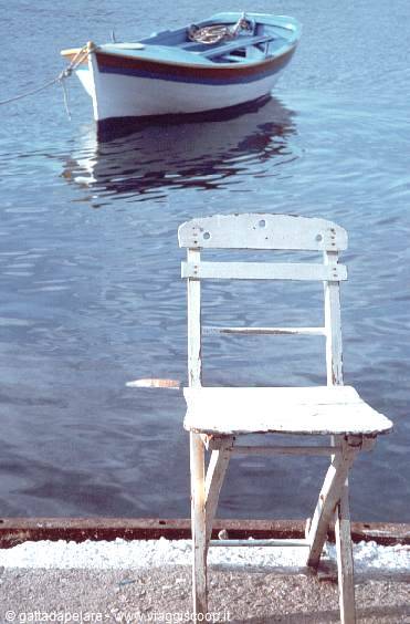 Weathered white chair on a dock, blue rowboat moored on calm water behind