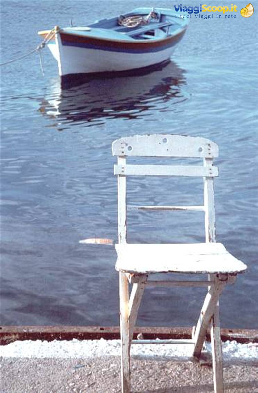 Weathered white chair on a dock, blue rowboat moored on calm water behind