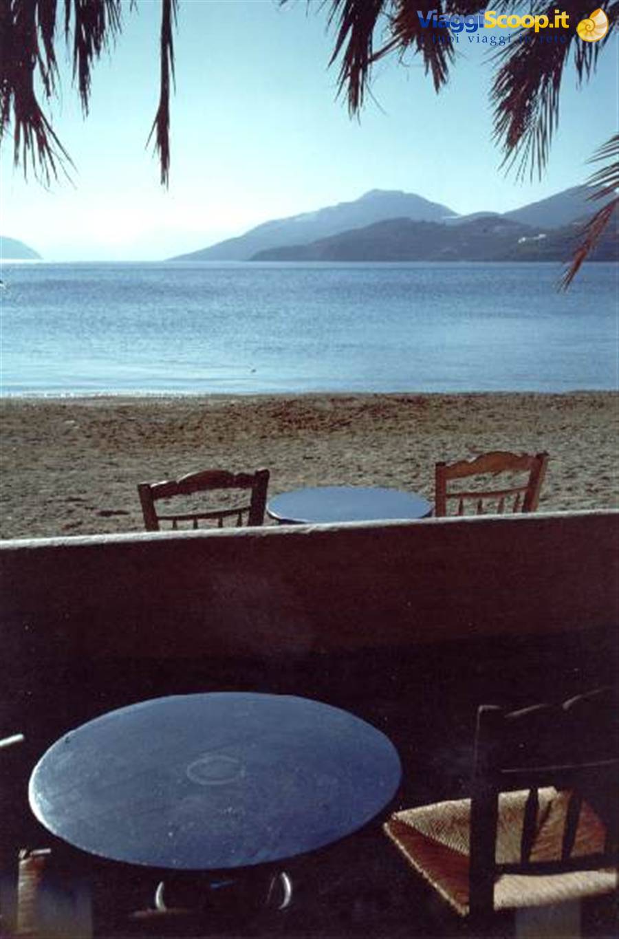 Empty wooden tables by the beach, blue sea and mountains across the bay