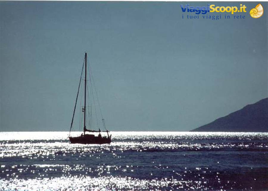 Sailboat silhouetted on sparkling sea, dark mountain on the horizon
