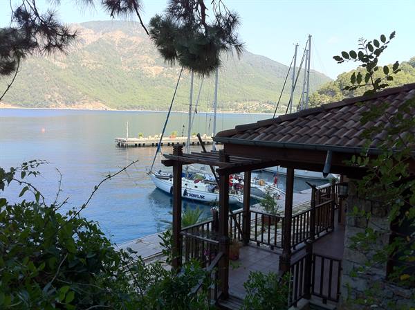 Sailboats moored at the pier beside a wooden terrace, green mountains bay