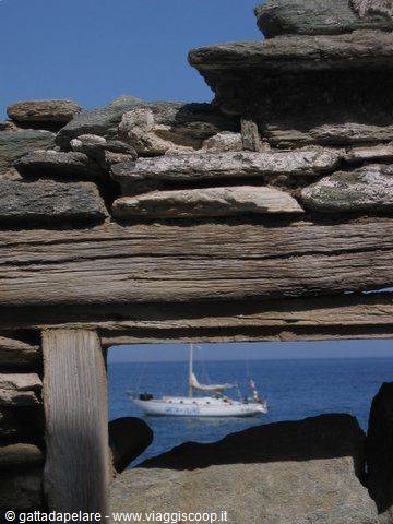 Sailboat framed by weathered stone wall, blue sea in the background