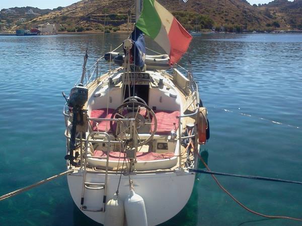 Sailboat flying Italian flag moored in turquoise bay among dry hills