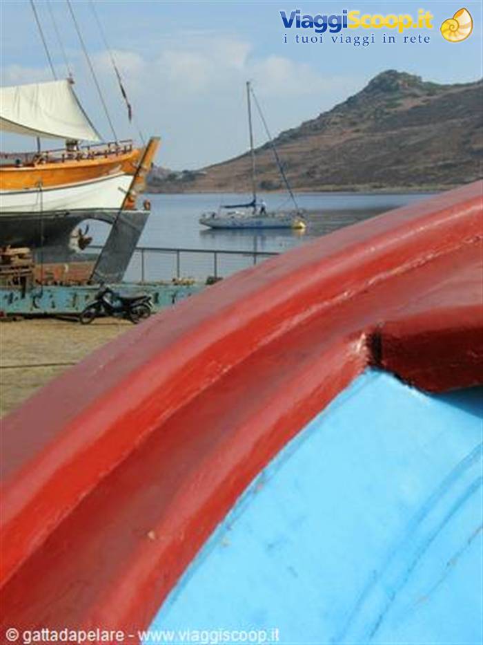 Red and blue boat bow, stranded tall ship and anchored sailboat in the bay
