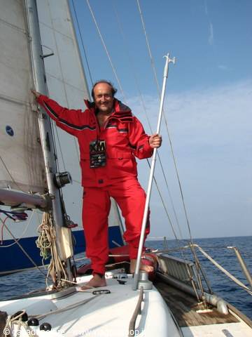 Man in red sailing suit on a sailboat at sea, gripping a pole