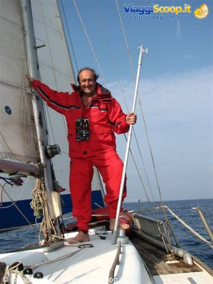 Man in red sailing suit on a sailboat at sea, gripping a pole