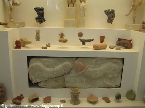 Museum display with stone relief and ancient pottery on lit shelves