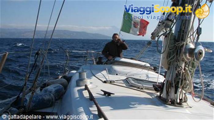 Man steering a sailboat flying the Italian flag, choppy sea, distant coast