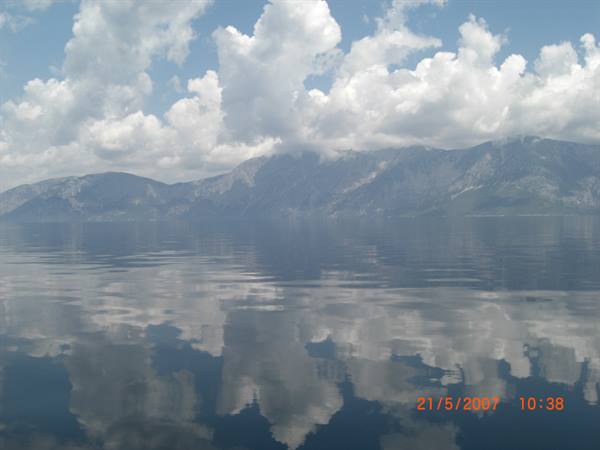 White clouds reflected on calm water in front of rocky mountains