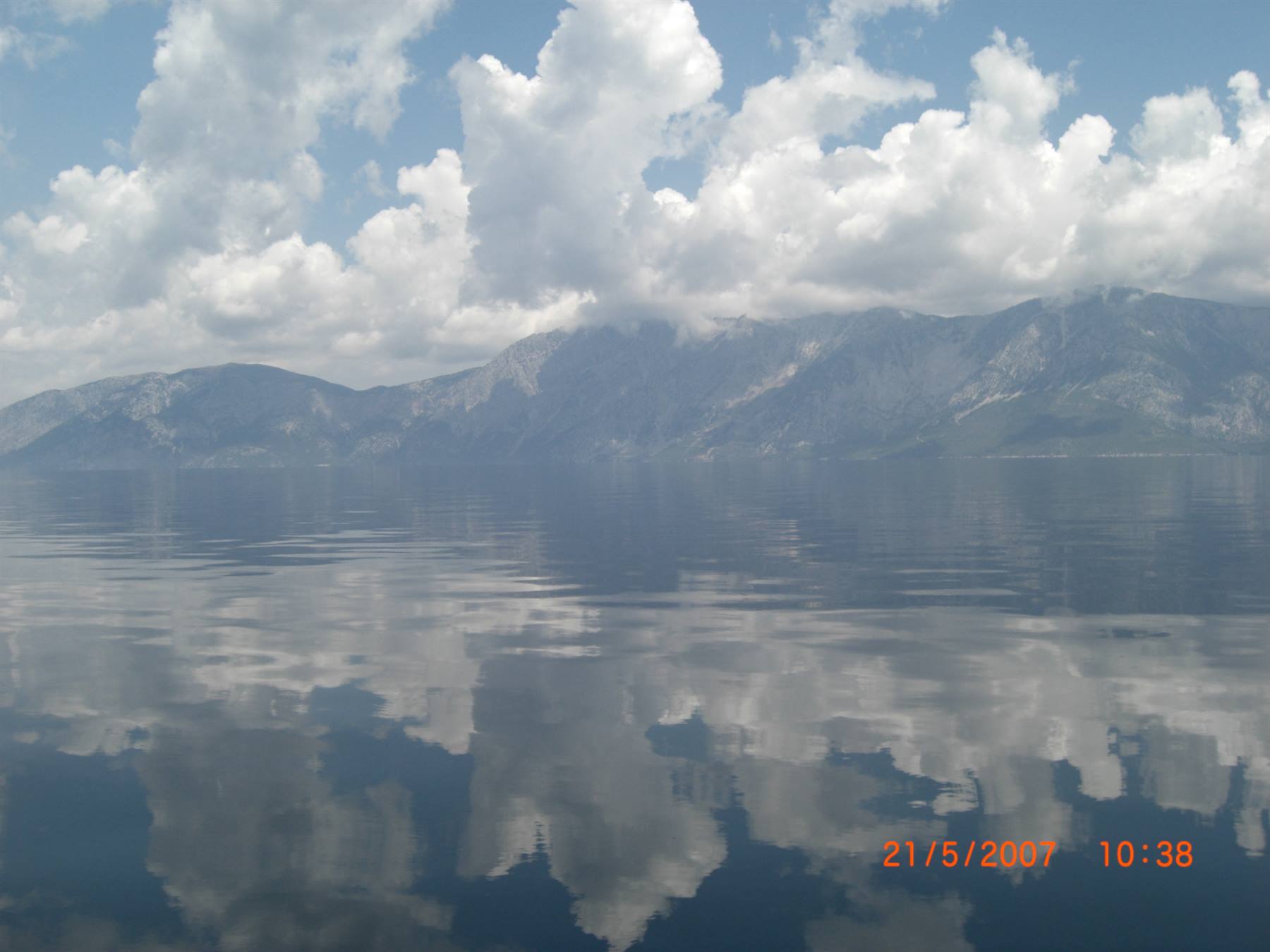 White clouds reflected on calm water in front of rocky mountains
