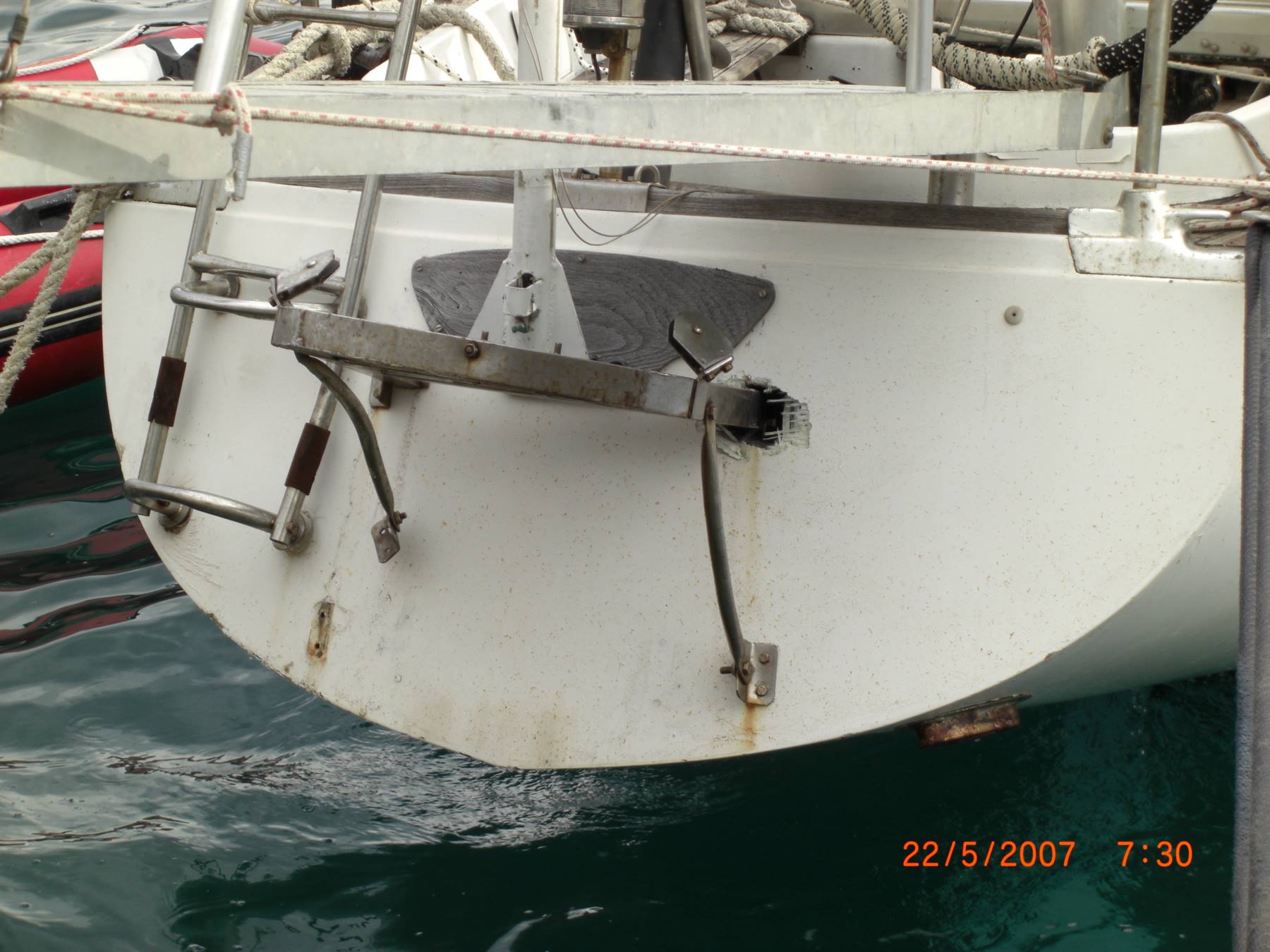 White sailboat stern with steel boarding ladder and rudder, moored at the harbor