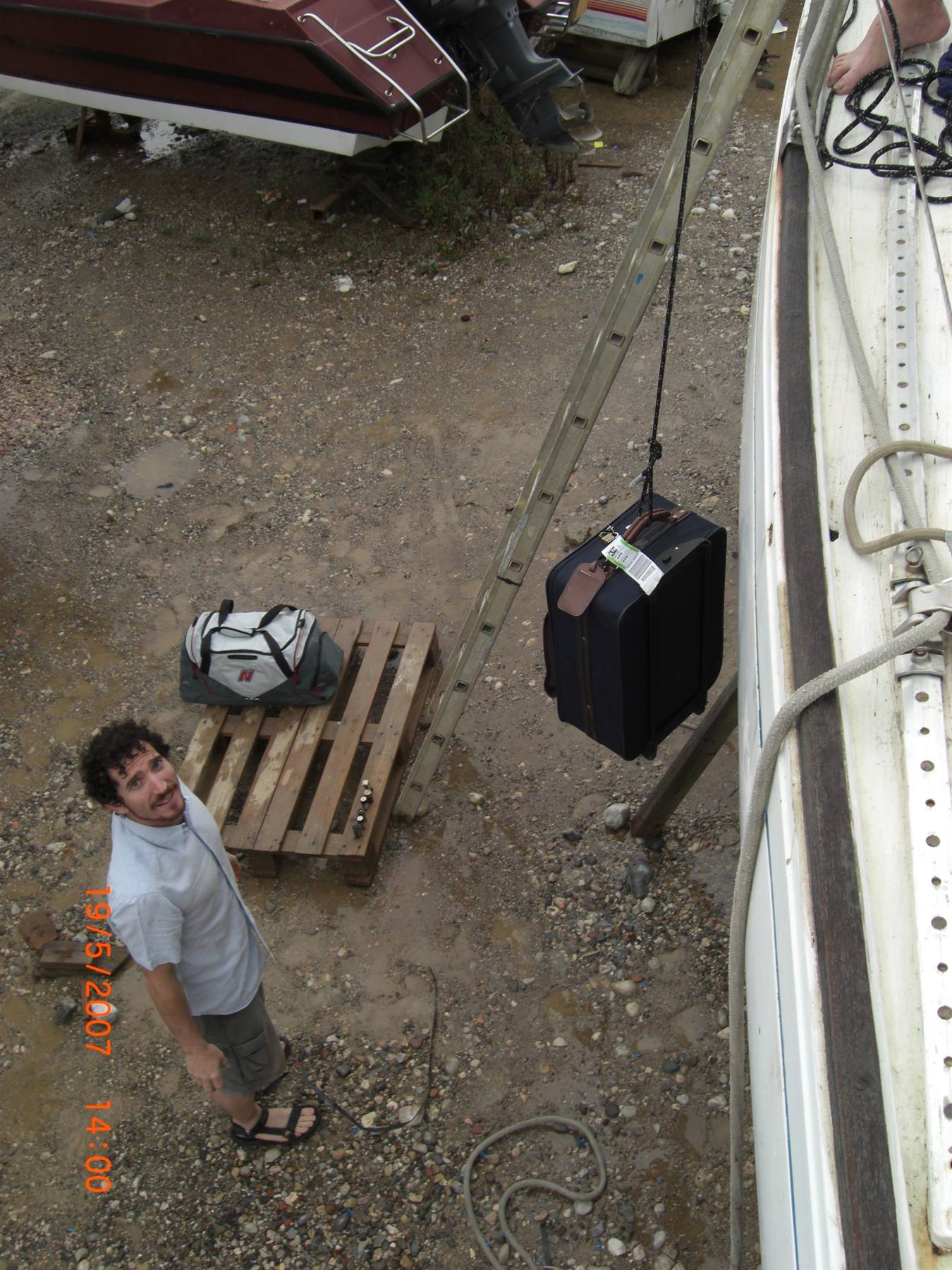 A man watches a suitcase hung from a spar beside the boat