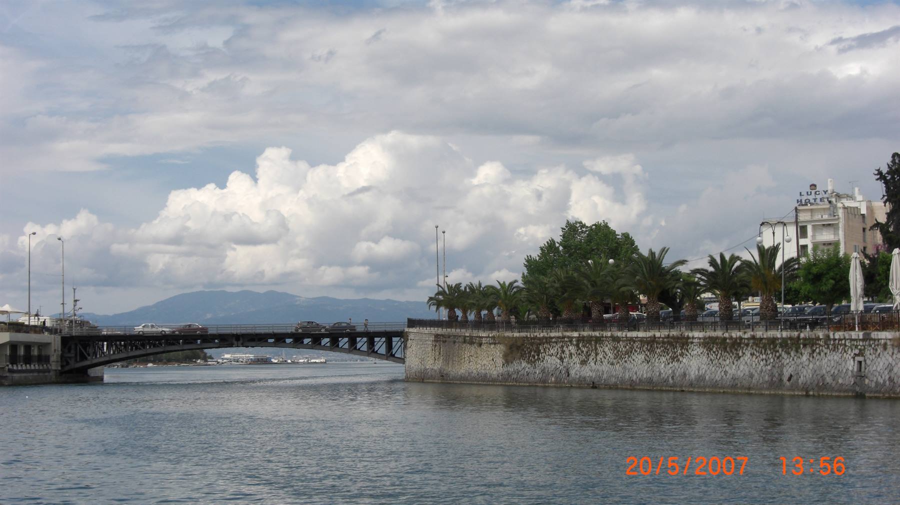 Iron bridge over water with palm trees and waterfront under white clouds