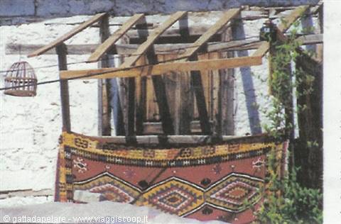 Red kilim rug hanging under a wooden beam pergola against a whitewashed wall