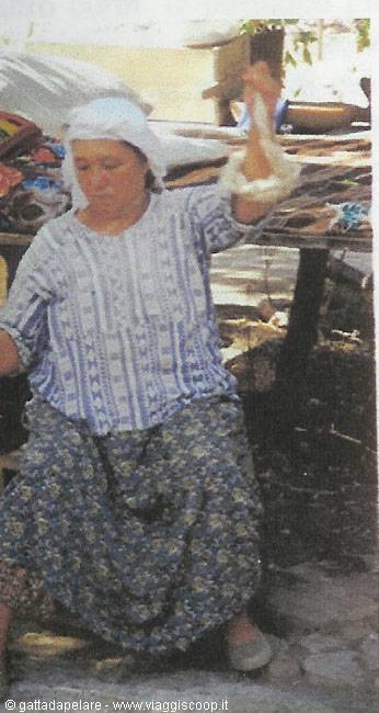Woman in white headscarf and floral skirt spinning thread at a market stall