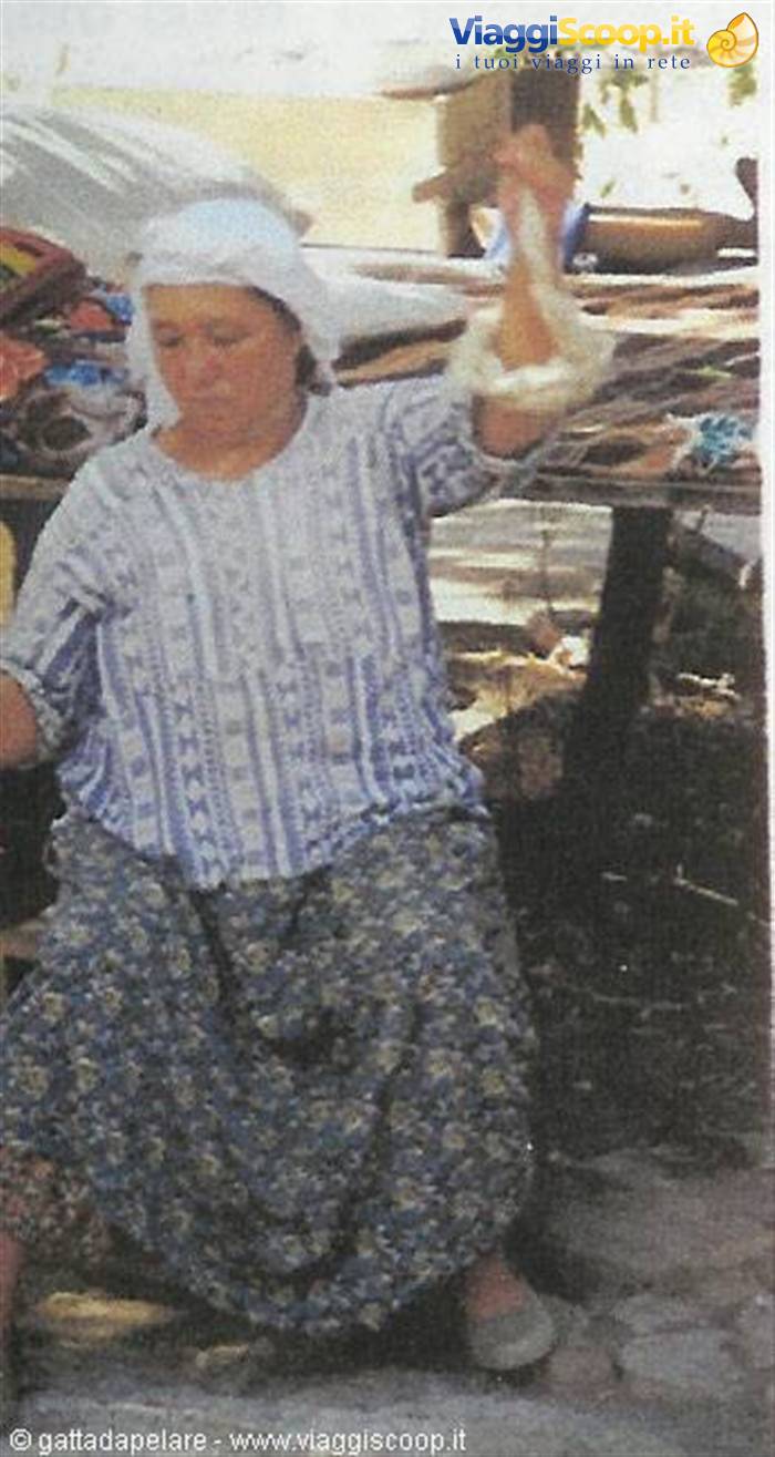 Woman in white headscarf and floral skirt spinning thread at a market stall