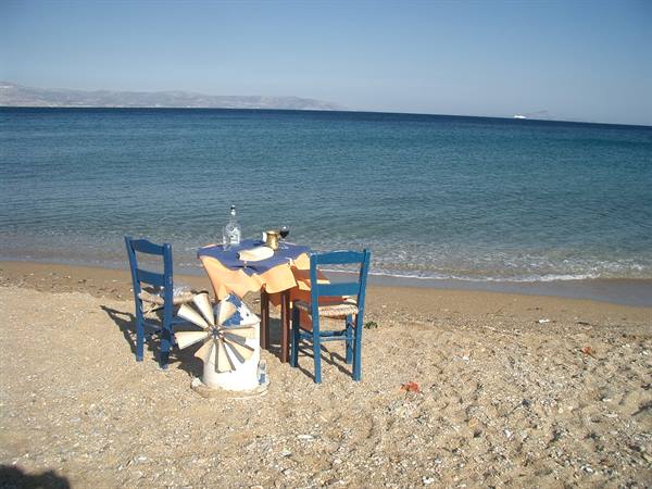 Table with wine and two blue chairs on the sand by the sea