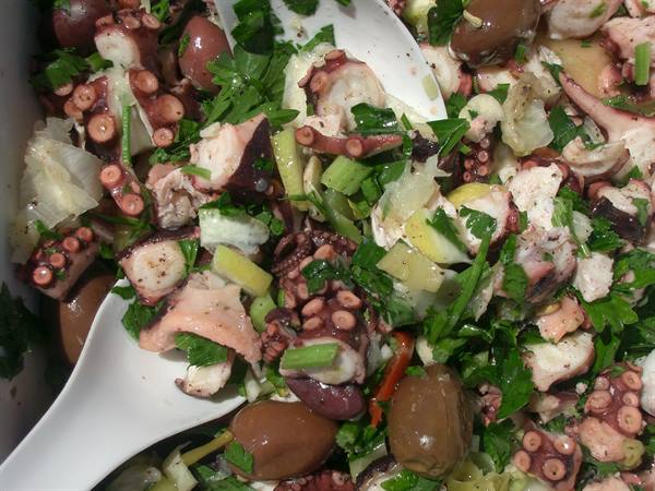 Octopus salad with olives, parsley and celery, white serving spoons close up