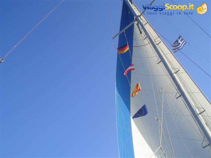 White and blue sail with international flags fluttering against clear blue sky