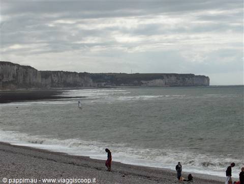 People walking on pebble beach below Yport chalk cliffs, overcast sky