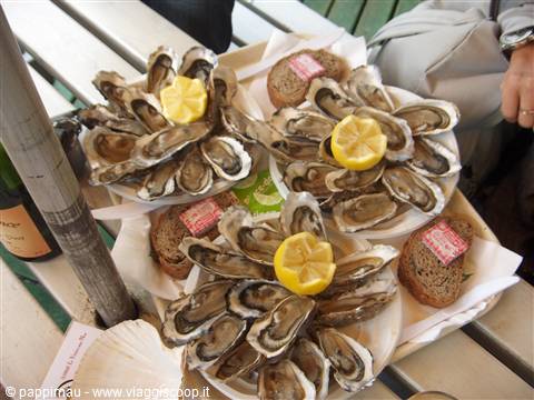 Platters of fresh oysters with lemon slices and rye bread at an outdoor stand