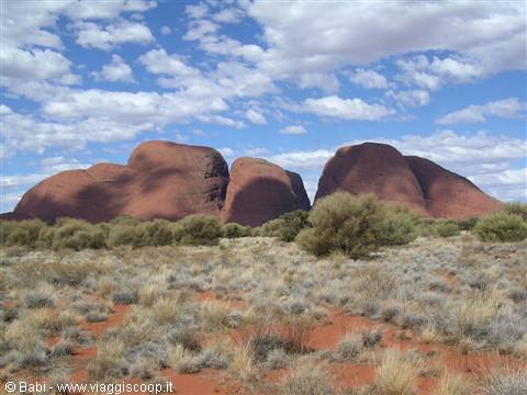 Red domes of Kata Tjuta rising over shrubs and sandy soil beneath white clouds