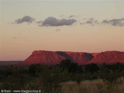 Red rock cliffs glowing at dusk above dry shrubs and dark trees
