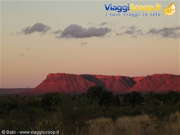 Red rock cliffs glowing at dusk above dry shrubs and dark trees