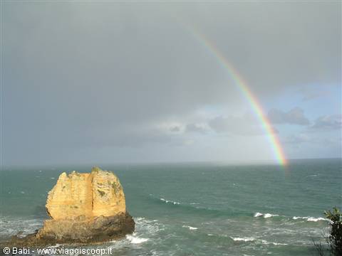Rainbow over the ocean above a golden rock stack, waves and clouds