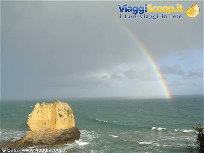 Rainbow over the ocean above a golden rock stack, waves and clouds