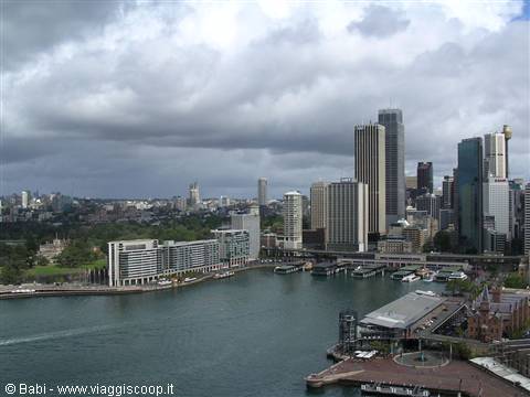 Sydney skyscrapers over Circular Quay under grey clouds, ferries docked along the bay