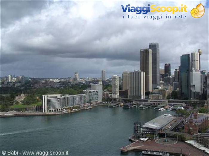 Sydney skyscrapers over Circular Quay under grey clouds, ferries docked along the bay