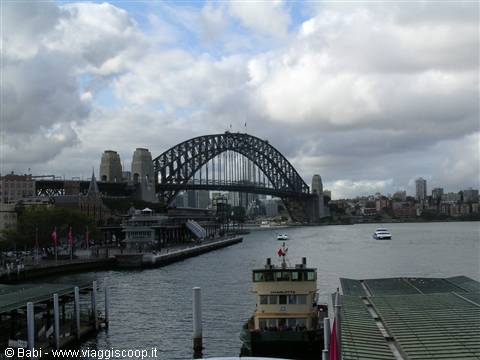 Ferry at the dock in front of Sydney Harbour Bridge under clouds