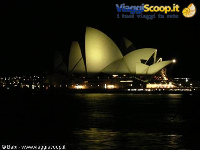 Sydney Opera House lit up at night, white sails reflecting on the water