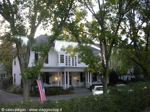 White wooden house with porch and American flag among tall trees