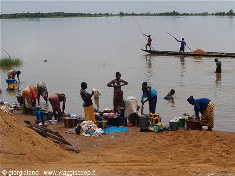 Women washing clothes on the sandy bank, fishermen in pirogue on the Niger River