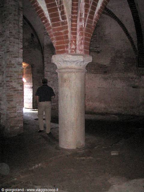 Man beside stone column and brick vault inside a dim crypt