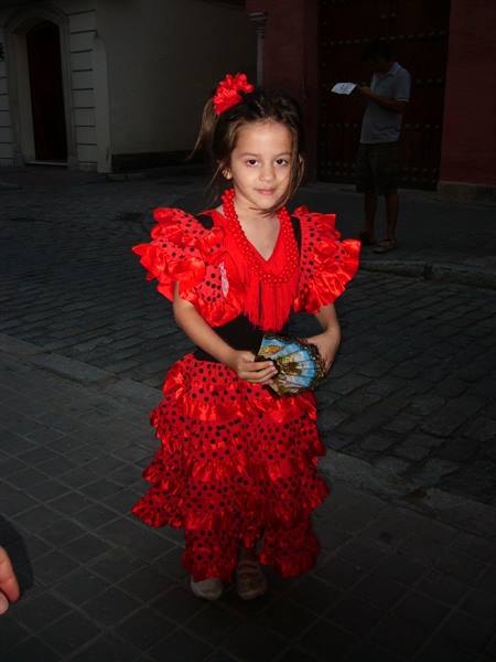 Little girl in red ruffled flamenco dress holding a fan on cobblestone street