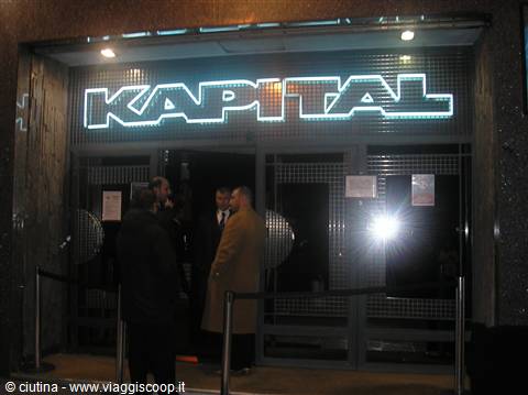 Glowing Kapital nightclub sign, men in coats chatting outside the dark entrance