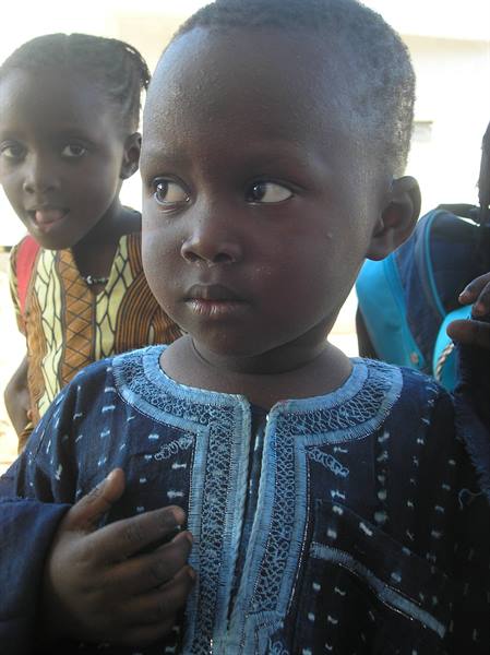 Boy in embroidered blue tunic glancing sideways, girl with backpack behind