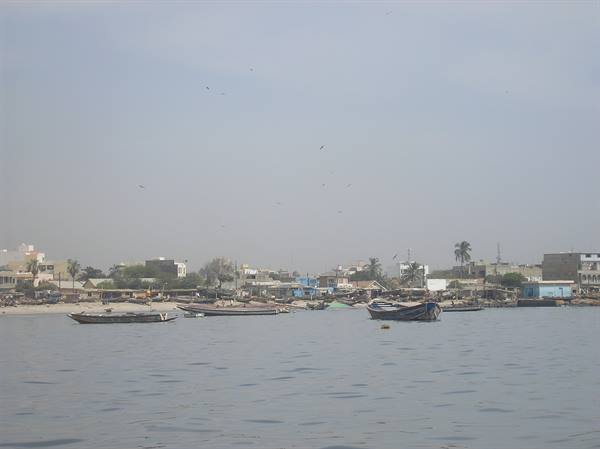 Fishing boats moored along the harbor shore under a hazy sky