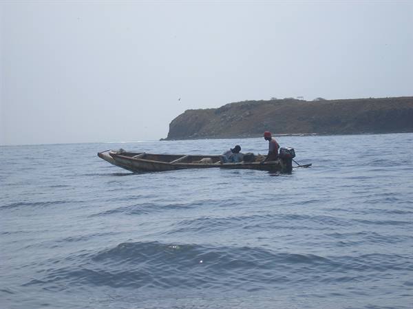 Fishermen in wooden boat with outboard motor near a rocky coast