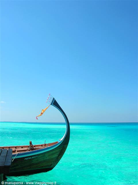 Wooden dhoni with curved bow moored on turquoise water under blue sky